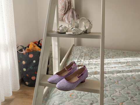 Girls glitter purple dress shoes and silver sandals displayed on white wooden ladder shelf in cozy children bedroom
