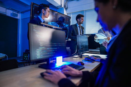 Professional developers coding and troubleshooting automotive software systems on screens in a high tech office at night.