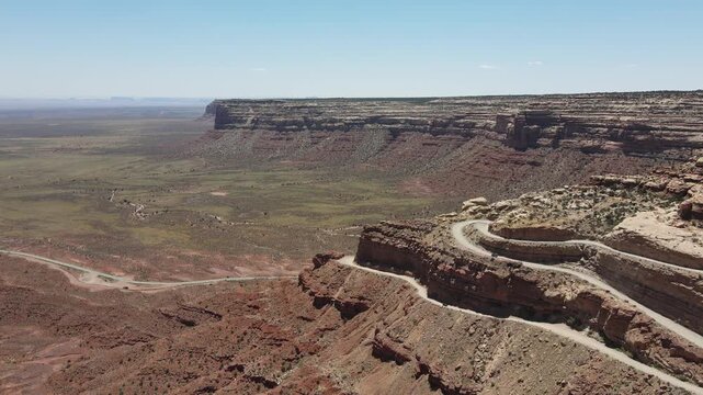 Professional 4K drone tracking shot moving right along the steep sandstone cliffs of Moki Dugway, Utah. The footage captures multiple cars navigating the winding dirt switchbacks of Highway 261.