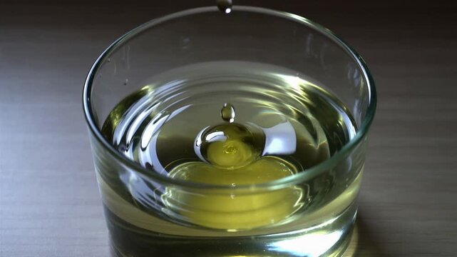 Close-up of a pickle submerged in a glass of clear liquid on a wooden surface with soft lighting.