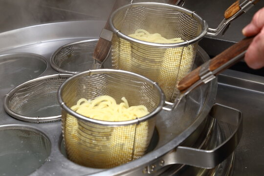 ゆで麺機で茹でられる中華麺のクローズアップと湯気