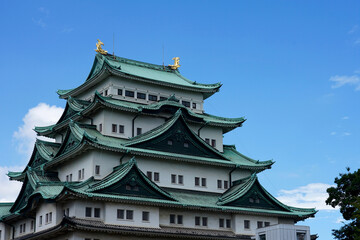 Fototapeta premium Traditional Japanese Castle With Layered Green Roofs Framed by Trees Under Blue Sky