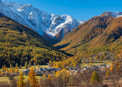 Autumn view of Le Casset village in the Guisane Valley, Ecrins National Park. French Alps with golden larch forest and snowy mountain peaks, Hautes-Alpes, France