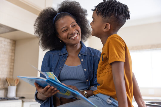 African American mother and son reading colorful picture book on kitchen counter smiling