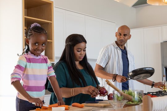 African American family chopping carrots, slicing red onion, holding frying pan at kitchen island