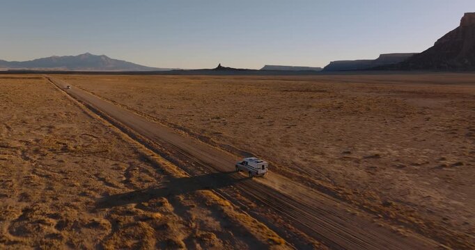Aerial medium tracking follow of vehicle driving across vast desert plain near Factory Butte Utah