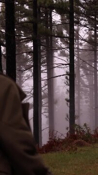 Joyful young woman running away from camera in misty pine forest in Tenerife, then turning around with a bright smile. Energetic lifestyle and travel content with cinematic foggy woodland.