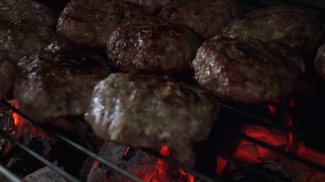 Juicy Grilled Meatballs Sizzling Over Glowing Charcoal Flames on Barbecue Grill. Close-up of Homemade Beef Burgers Sizzling on a Barbecue Grill