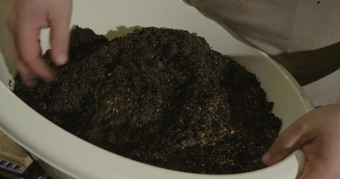 Closeup of a gardener's hands mixing fertile potting soil with amendments in a white basin, preparing a nutritious substrate for planting flowers, vegetables, or houseplants at home.