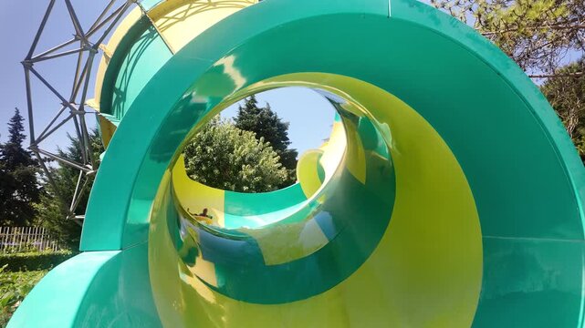 Happy girl riding down on colorful water slide at Aquapark. Little girl at water park. Summer vacation fun, adventure, and recreation at an aquapark.