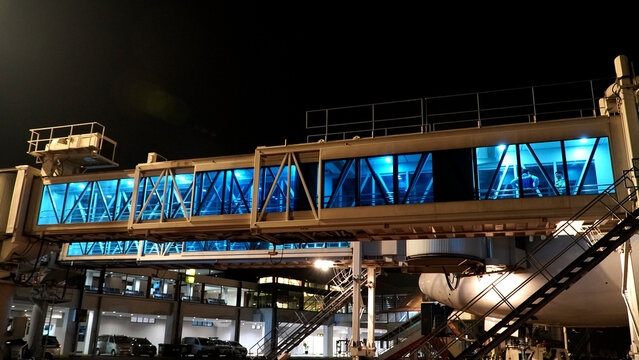 Modern airport jet bridge with blue interior lighting at night perspective view of passenger boarding bridge at terminal gate for aircraft connection aviation facility