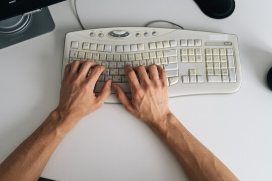 Top down view of male hands typing on old beige computer keyboard. Minimalist white desk setting with bright, even light. Concept for work, business, programming, writing, or technology.