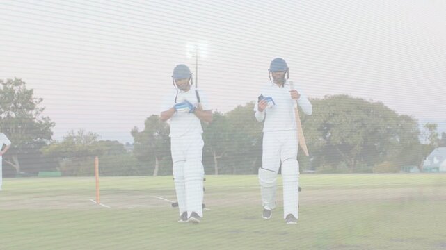 Cricket batsmen talking, bumping fists after milestone, holding helmets and bats walking off pitch