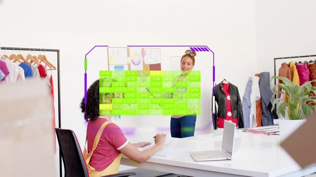 Standing woman tapping tablet rotating fashion holo chart while seated woman taking notes reviewing