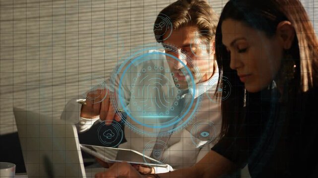 Man pointing at laptop while woman typing, causing biometric HUD over tablet protecting data