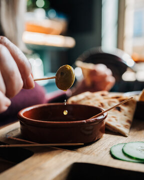 person holding an olive with oil dripping sat in a cafe