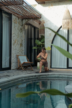 Woman kneeling in yoga pose with prayer hands at villa pool, Bali