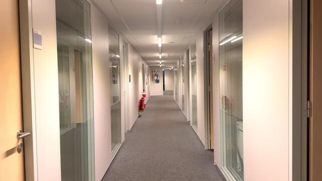 POV shot moving through a long, empty modern office hallway. Smooth tracking shot in a corporate building interior.