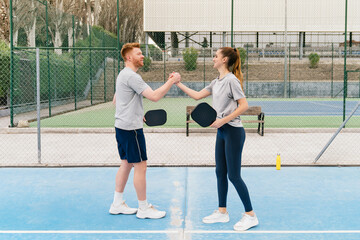 Fototapeta premium Two pickleball players demonstrating sportsmanship, handshaking and holding paddles on a vibrant blue court after their game