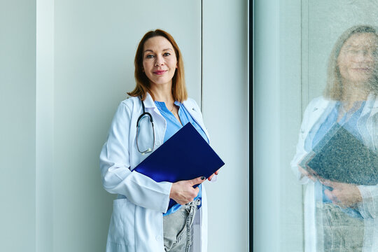 Confident doctor in lab coat holding a folder indoors at hospital