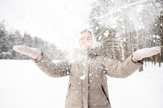 Smiling while throwing snow in the air wearing warm clothing