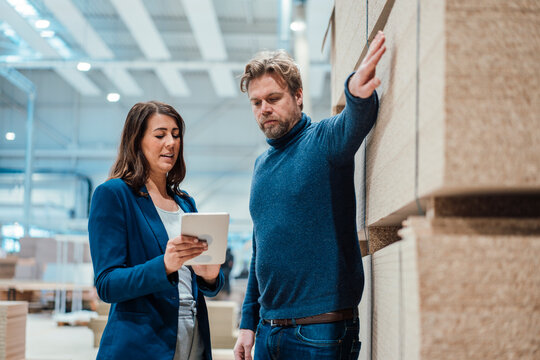Businesswoman sharing tablet PC with colleague by wooden planks in workshop