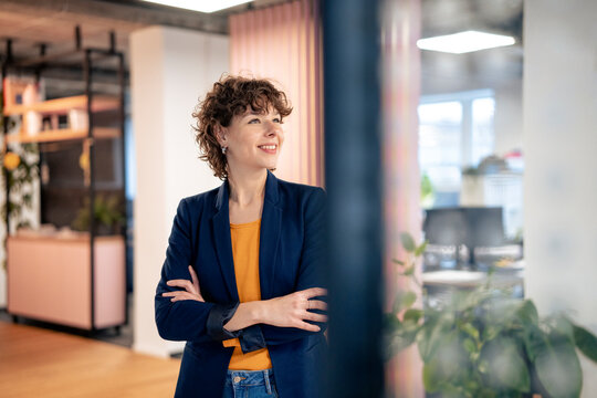 Smiling young businesswoman standing with arms crossed at office
