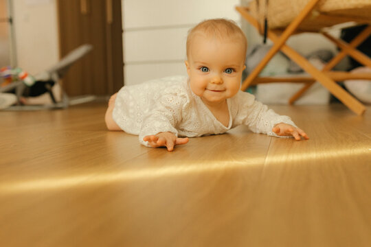 Smiling baby crawling on a sunlit wooden floor indoors