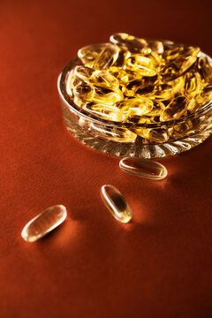 Golden omega 3 vitamin capsules in a glass bowl on red background