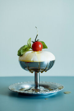 Fresh burrata with tomato and basil in a metal cup on a blue table