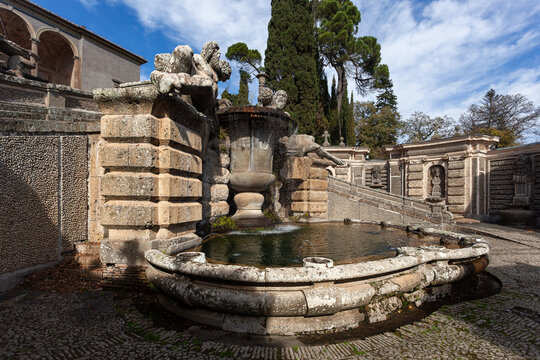 Renaissance stone fountain with sculptures and flowing water in the gardens of Villa Farnese, Caprarola, Italy. Historic monumental architecture with tall cypress trees.