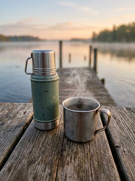 Green thermos and a steaming metal cup on a wooden dock