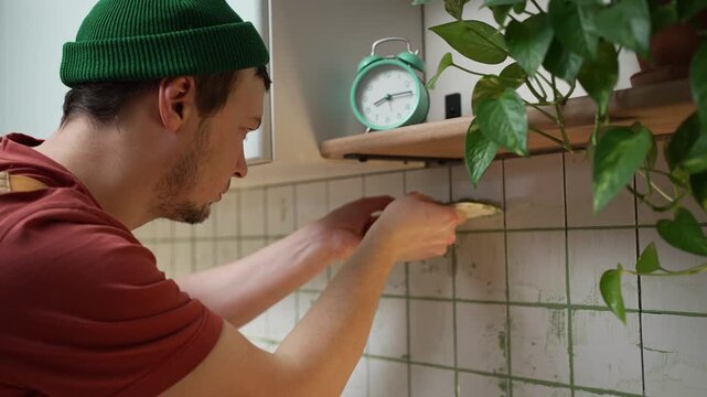 Meticulous construction worker carefully applying green grout into the joints of white kitchen backsplash tiles, focusing on the detailed process of home renovation and interior design