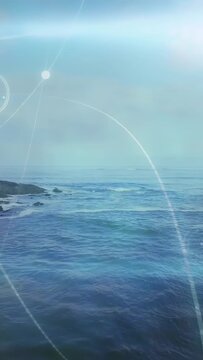 Vertical video: Horizon glare rising, sparking rings and orbs sweeping over calm sea, tinting surf