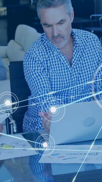 Vertical video: Lead typing laptop while team tapping tablet causing nodes crossing business charts