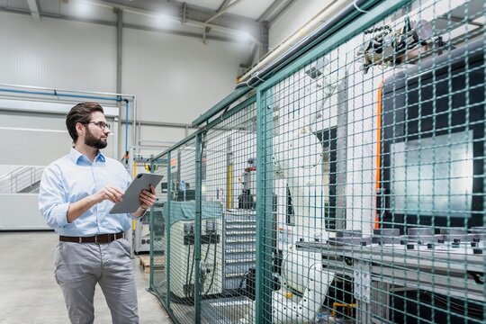 Engineer holding tablet PC and examining machines at factory