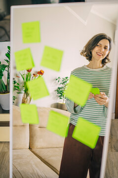 Woman reading positive affirmation note on mirror at home
