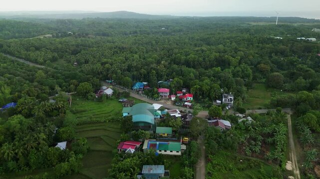 Aerial overview of a small rural village with colorful rooftops surrounded by dense tropical forest in Guimaras, Philippines.
