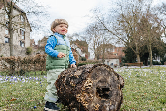 Smiling toddler standing next to a large log in a spring park