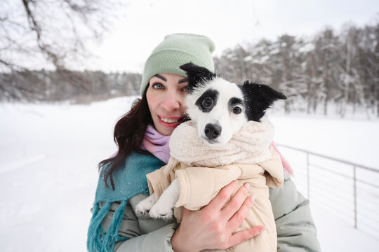 Woman holding her dog outdoors in warm clothes on a snowy winter day