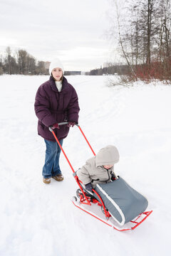 Mother pushing her son in a sled through the snow