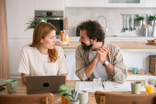 Couple talking and working together with laptop at home kitchen table