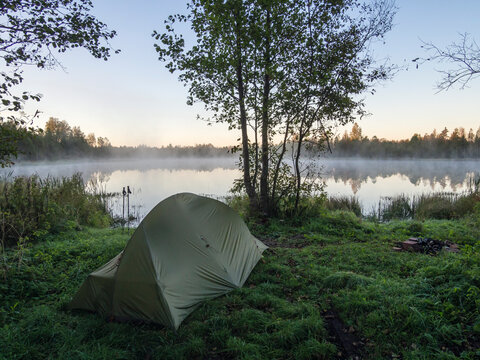 Green tent on the shore of a foggy lake in Estonia at dawn