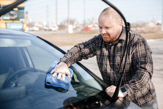 Driver cleaning car windshield with microfiber cloth outdoors