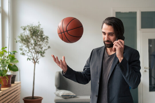 Businessman talking on smartphone and tossing basketball in mid-air at office