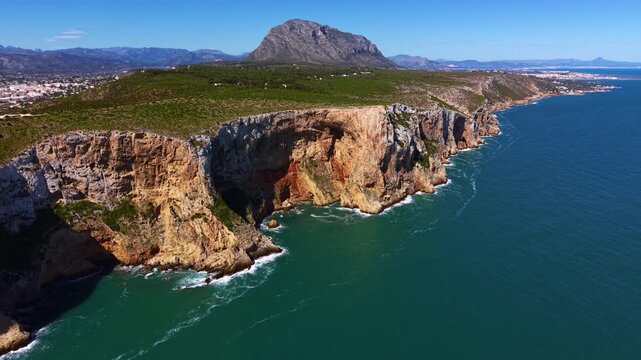 Moraira headland peninsula on the Costa Blanca, Spain, showing dramatic limestone cliffs dropping into turquoise Mediterranean Sea with mountains and coastline beyond