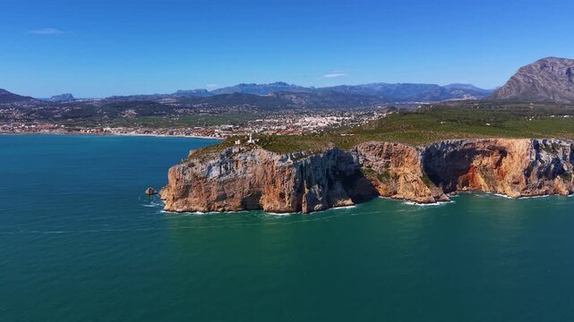 Moraira headland peninsula on the Costa Blanca, Spain, with dramatic limestone cliffs rising from turquoise Mediterranean waters, coastal town and mountains beyond