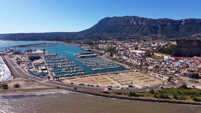 Xabia marina and coastal town on the Spanish Mediterranean coast with boats moored in harbour, palm-lined promenade and rocky mountains in the background