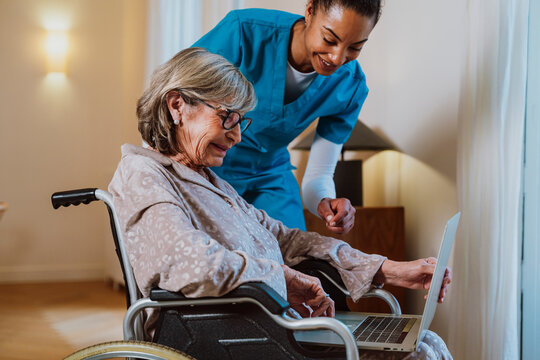 Caregiver assisting woman in wheelchair with laptop at home