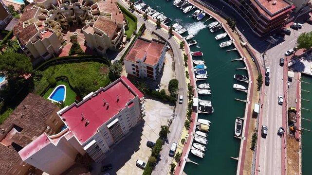 Overhead view of Xabia marina channel in Spain with moored boats lining both sides of a curving waterway surrounded by residential buildings and roads